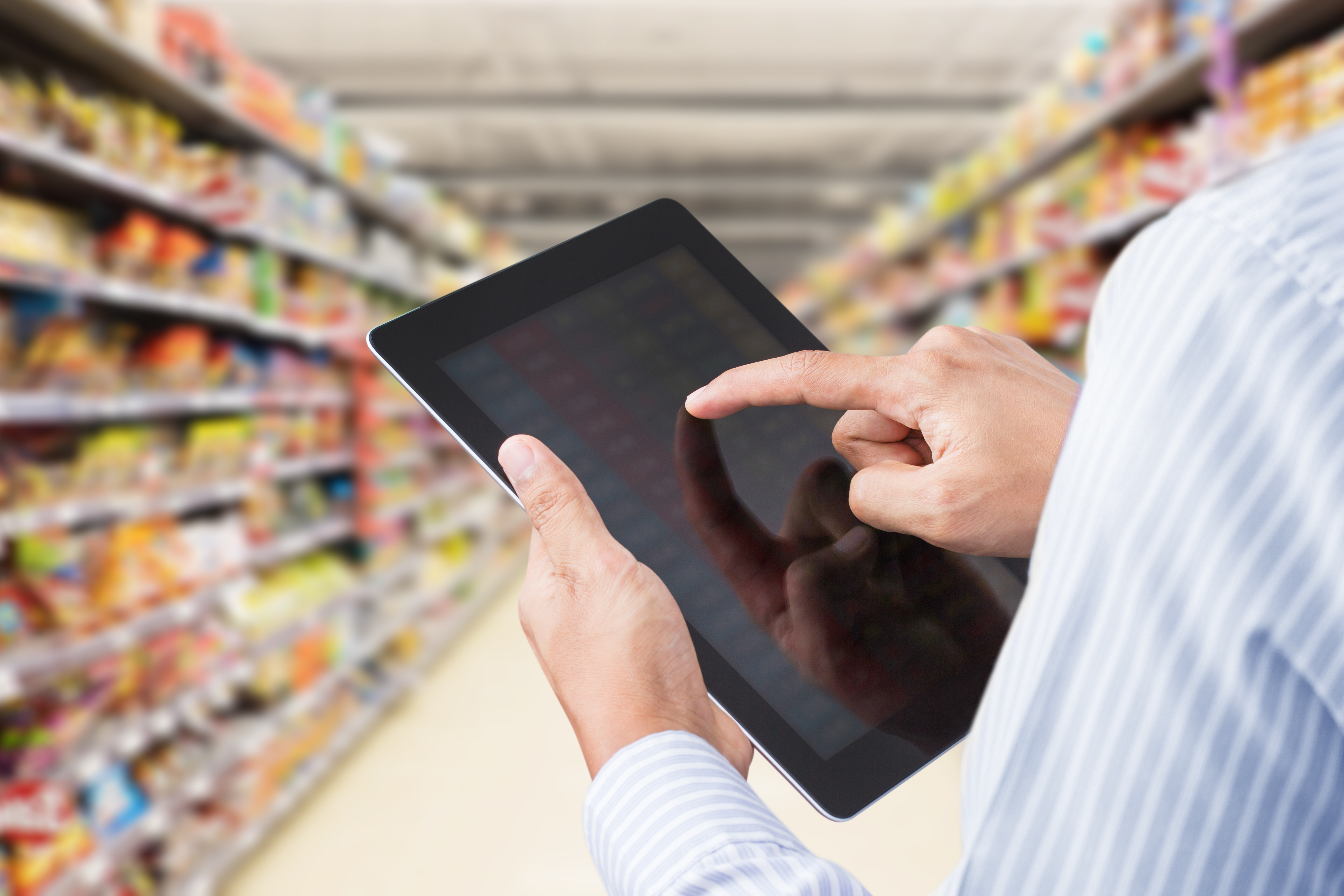 a worker using a tablet in grocery store aisle