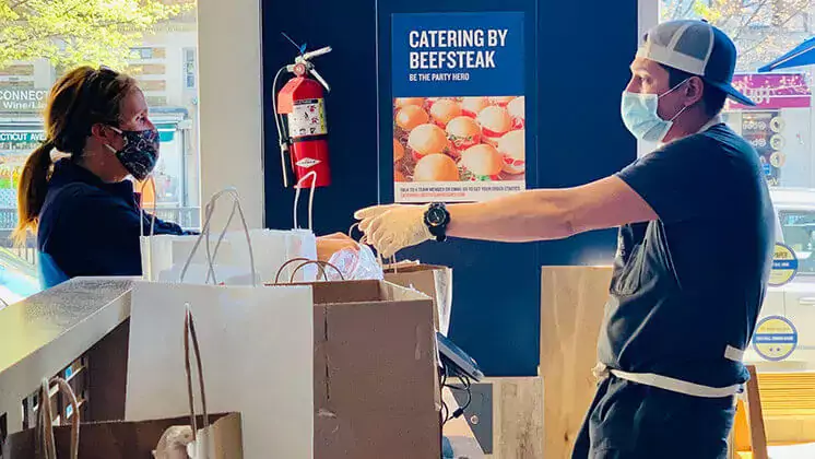 restaurant worker wearing mask and handing over to-go orders to another person wearing mask