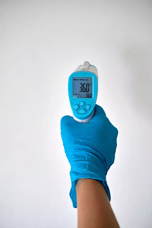 A hand with a blue glove holding a thermometer.